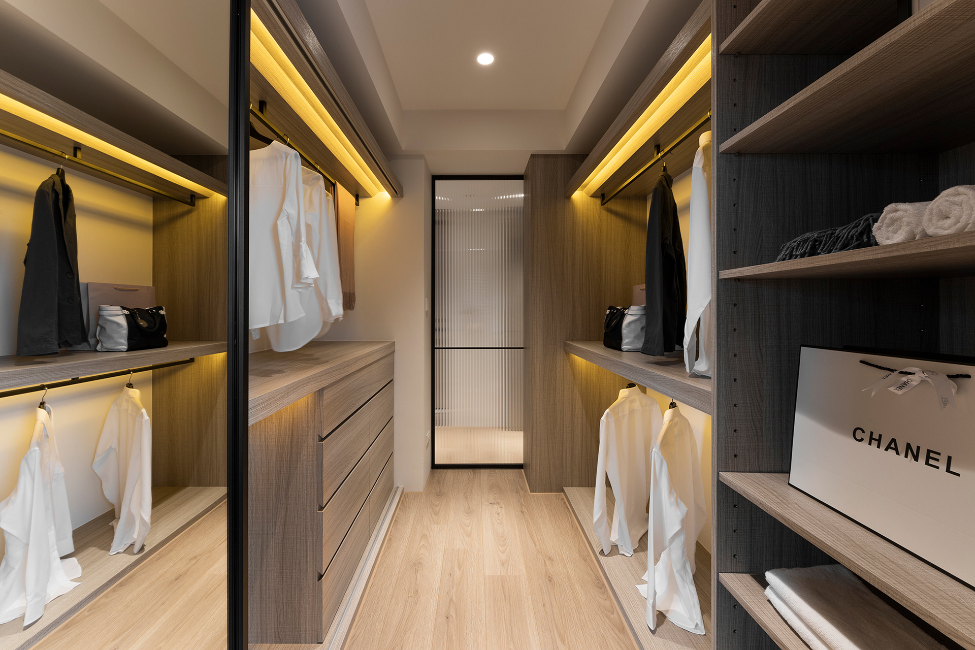 Well-organized walk-in closet with wood finishes and accent lighting.